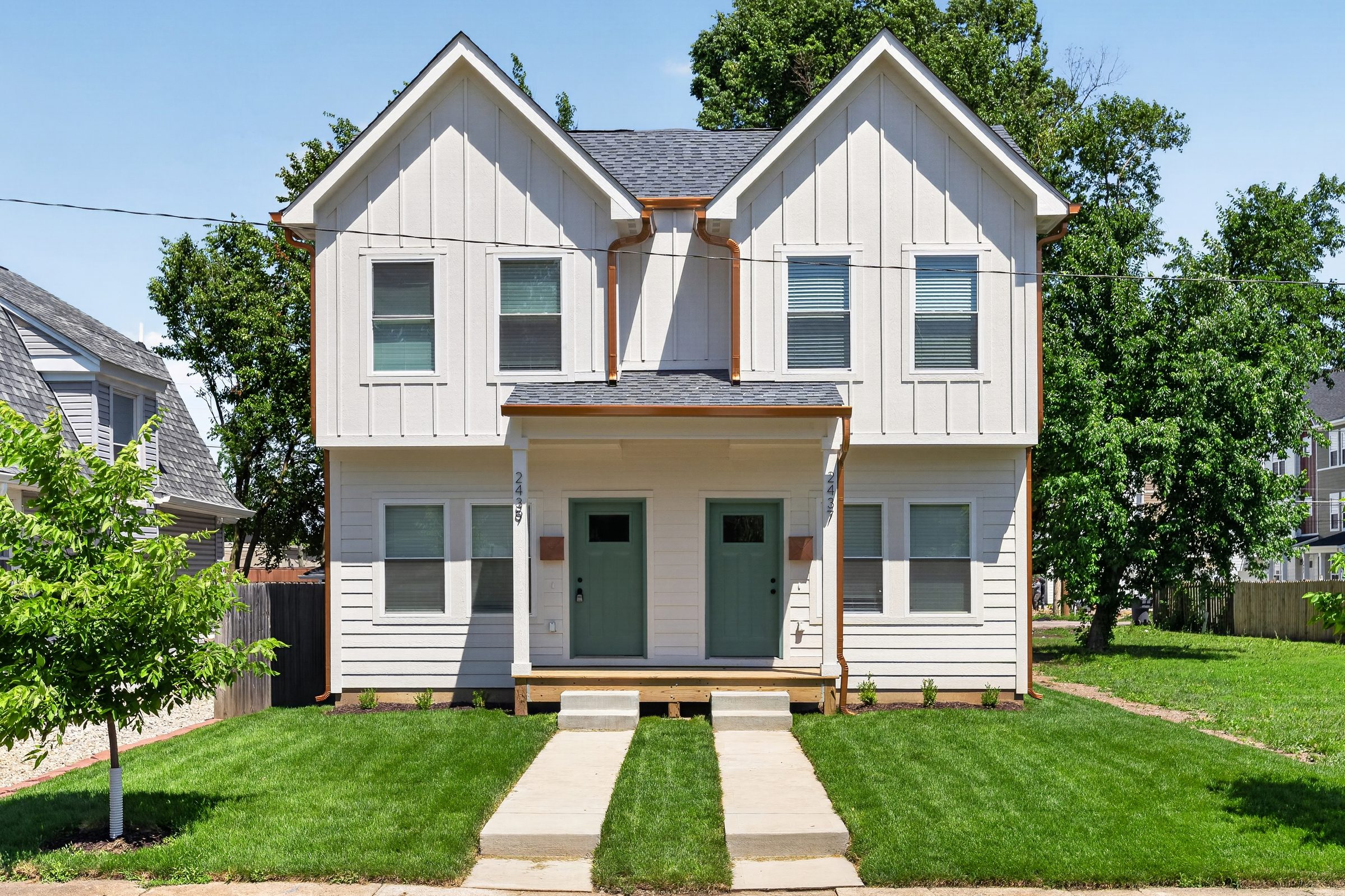 Front of the white board-and-batten duplex with two green doors